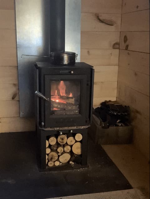 The small wood stove in the cabin, lit, with a pot warming on top